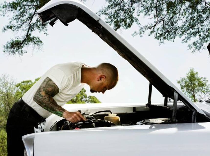 Un hombre trabaja en el cofre de su camioneta, dando mantenimiento a su motor.