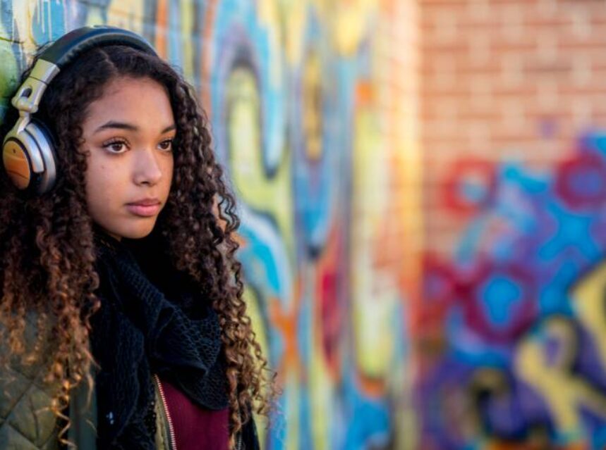 Joven adolescente con audífonos con un mural de graffiti de fondo.