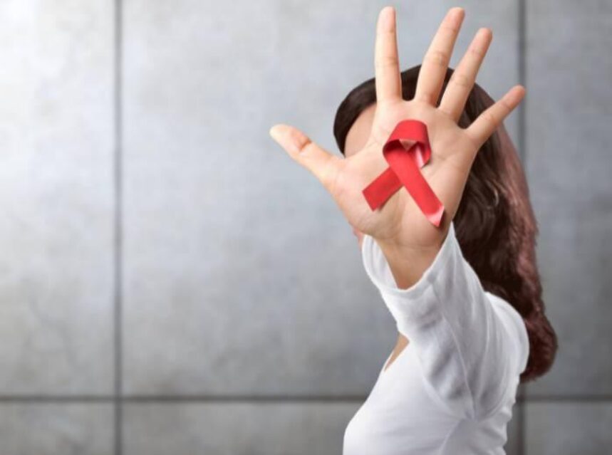 Mujer muestra la palma de su mano izquierda con un listón rojo en señal de la lucha contra el VIH SIDA.