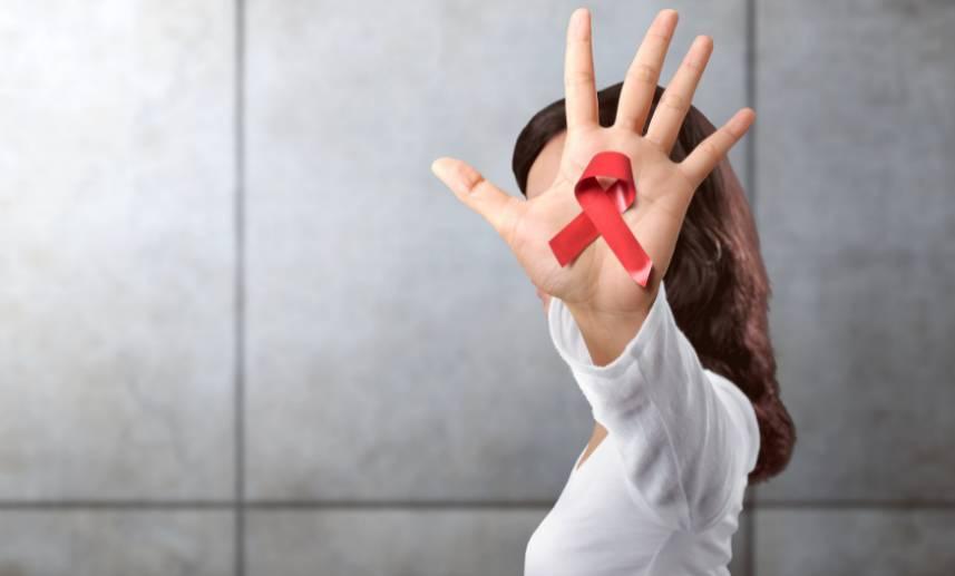 Mujer muestra la palma de su mano izquierda con un listón rojo en señal de la lucha contra el VIH SIDA.