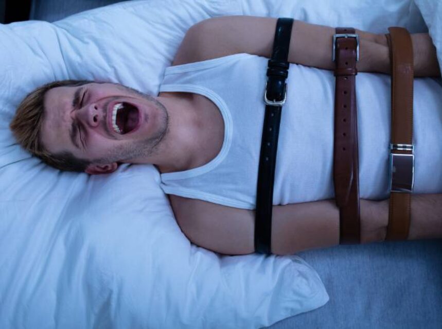 Hombre grita en cama con sujetadores de seguridad.