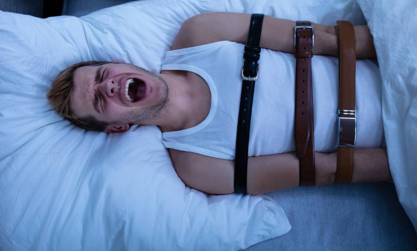 Hombre grita en cama con sujetadores de seguridad.