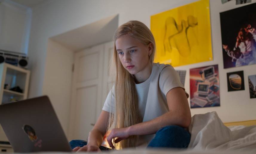 Una adolescente está sentada en su cama mientras mira su computadora.