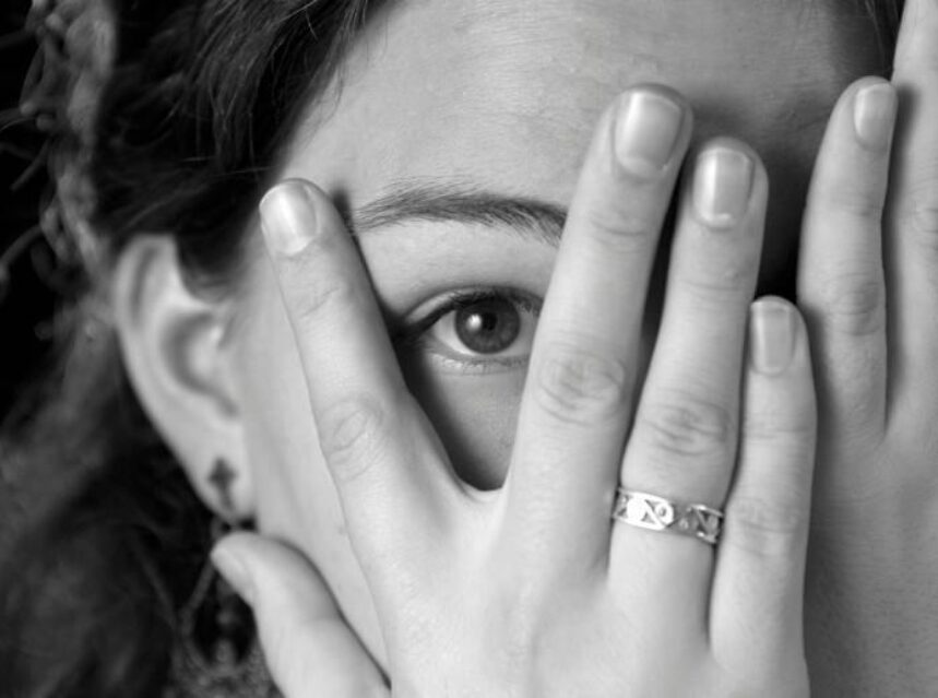 Rostro de mujer cubierto con su mano derecha, solo deja ver el ojo derecho en una apertura de los dedos.