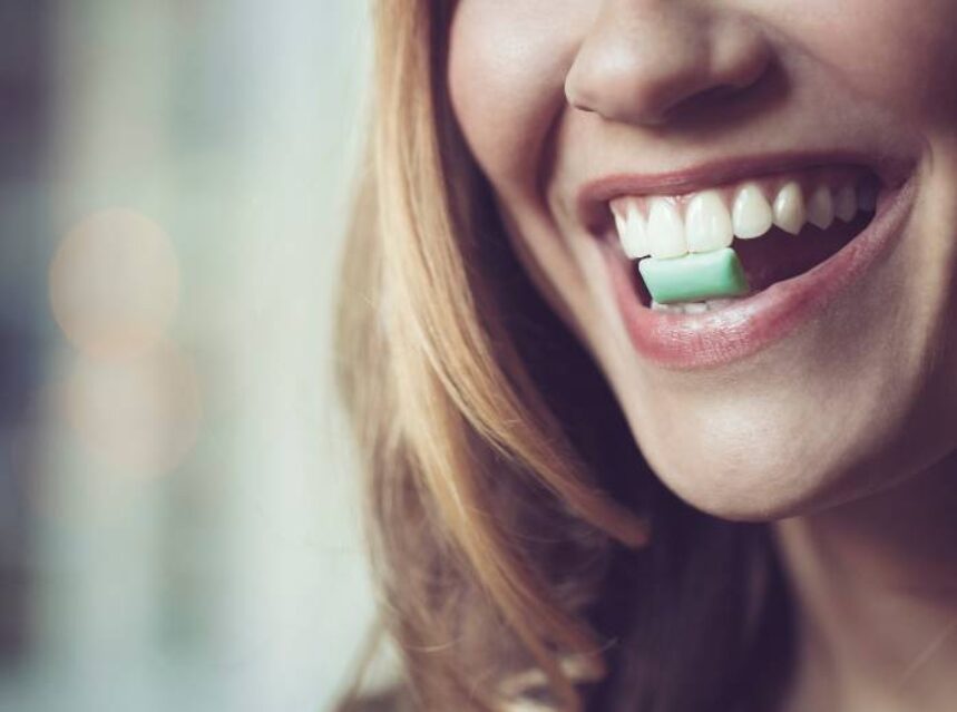 Rostro de mujer sonriente con una pastilla de goma de mascar en la dentadura.