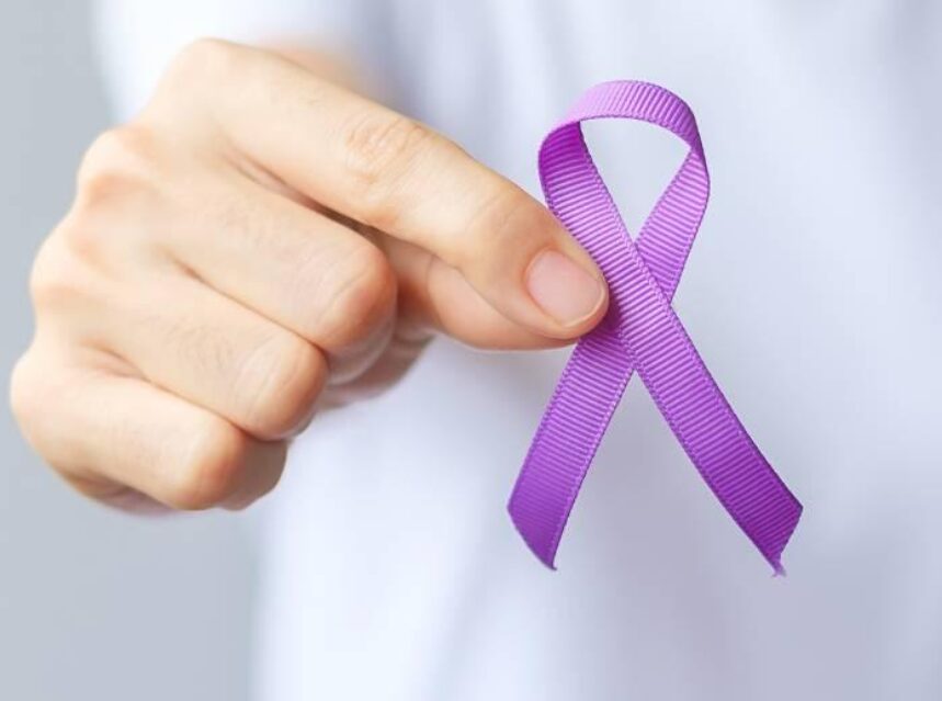 Una mano sostiene un listón morado en señal de apoyo a la prevención al cáncer de pancreas.