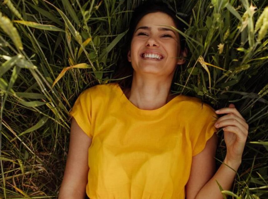 Mujer alegre y sonriente recostada en el pasto verde y largo.