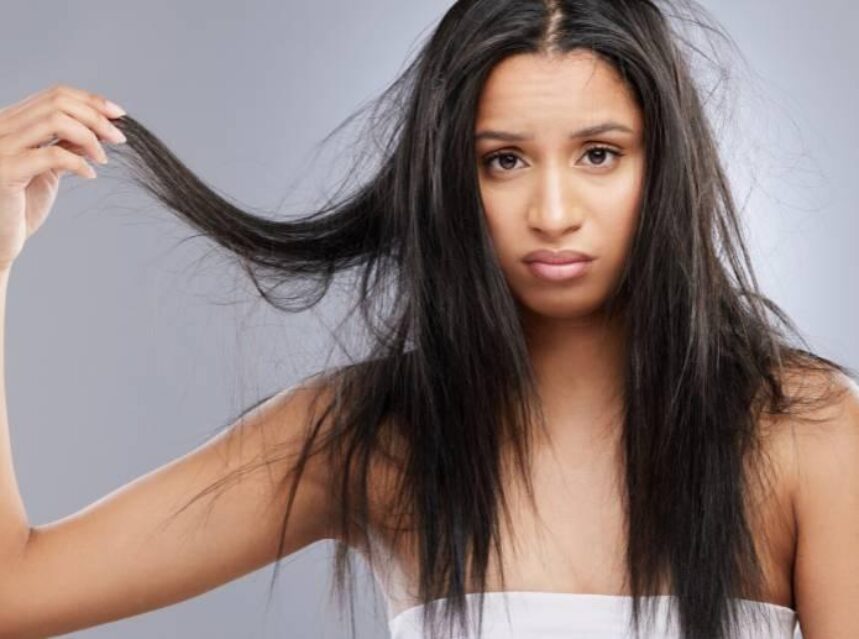 Mujer toma una parte de su cabello con frizz, haciendo una mueca en el rostro de insatisfacción.