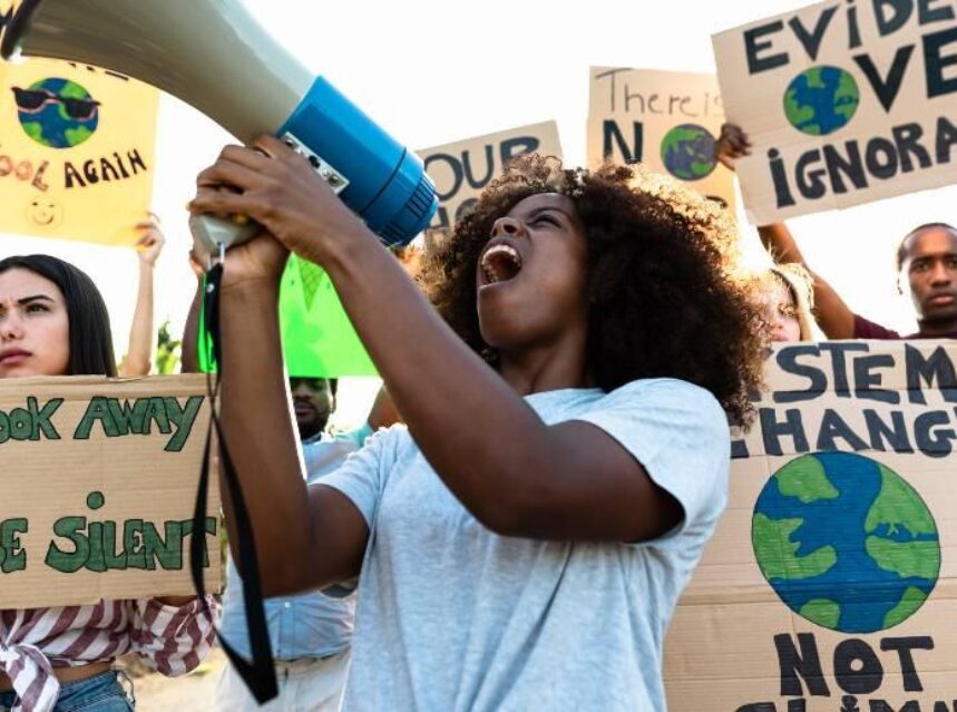 Mujer sostiene un megáfono mientras con otro grupo de personas tienen una manifestación pacífica a favor del medio ambiente.