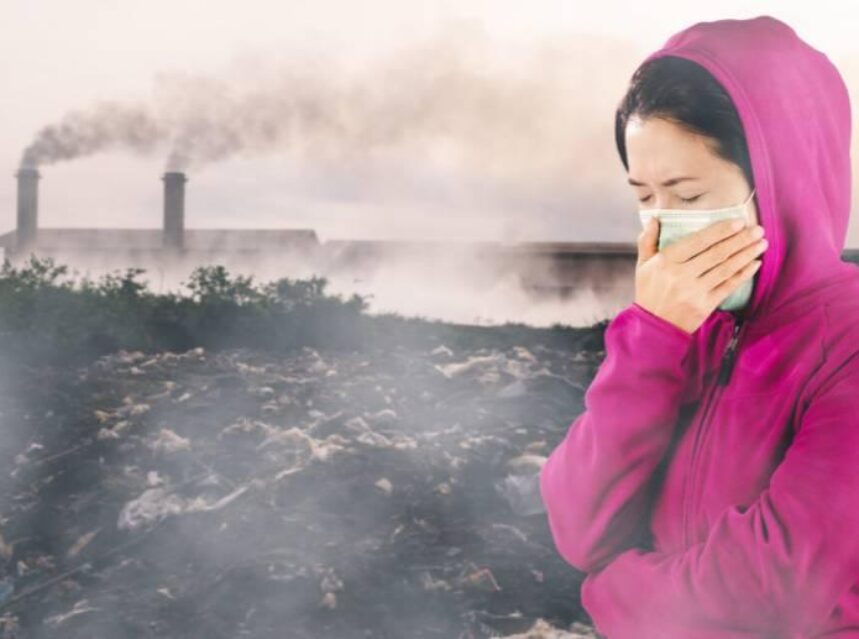 Mujer con cubrebocas, al fondo sale humo de una fábrica.