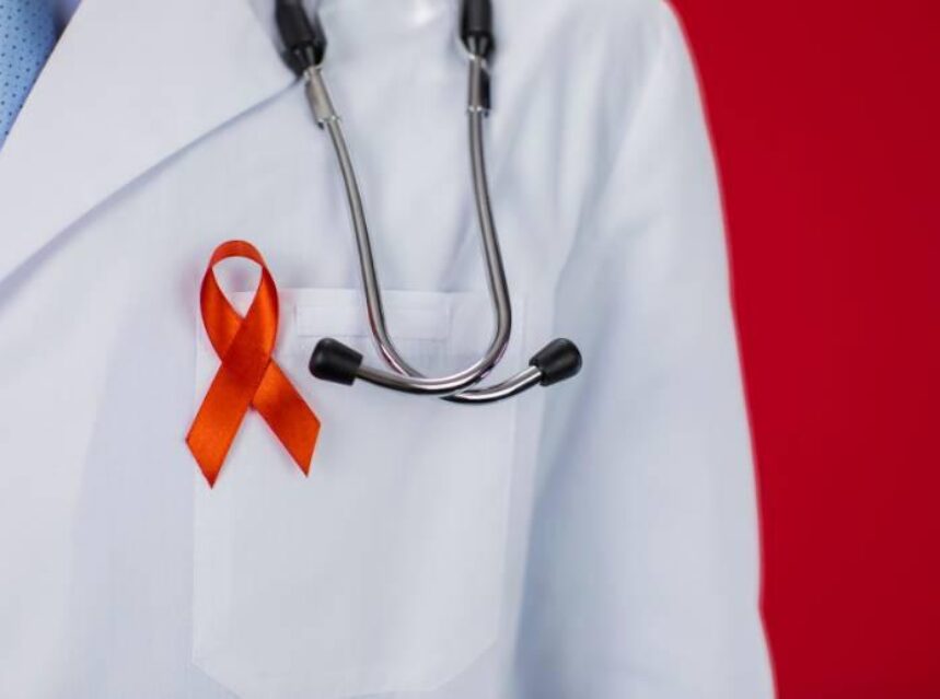Lado superior de una persona con bata de médico con un listón rojo símbolo de la lucha contra el VIH y SIDA.