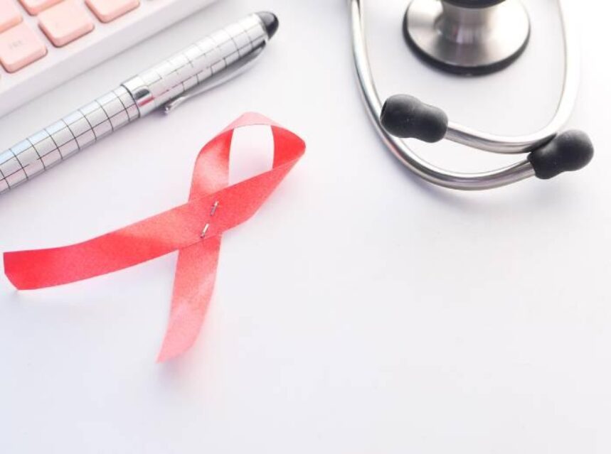 Imagen del símbolo de listón rojo de lucha contra el VIH, junto a una lapicera y equipo médico.