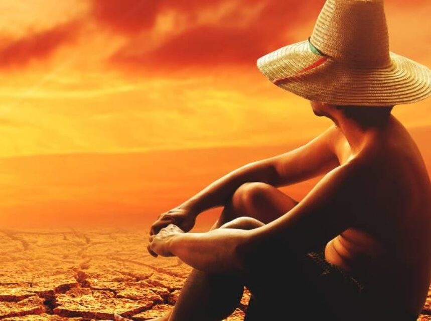 Hombre sentado en un desierto agrietado por sequía.