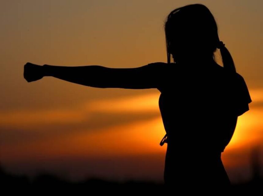 Mujer estira puño como entrenando boxing, al fondo una puesta de sol.