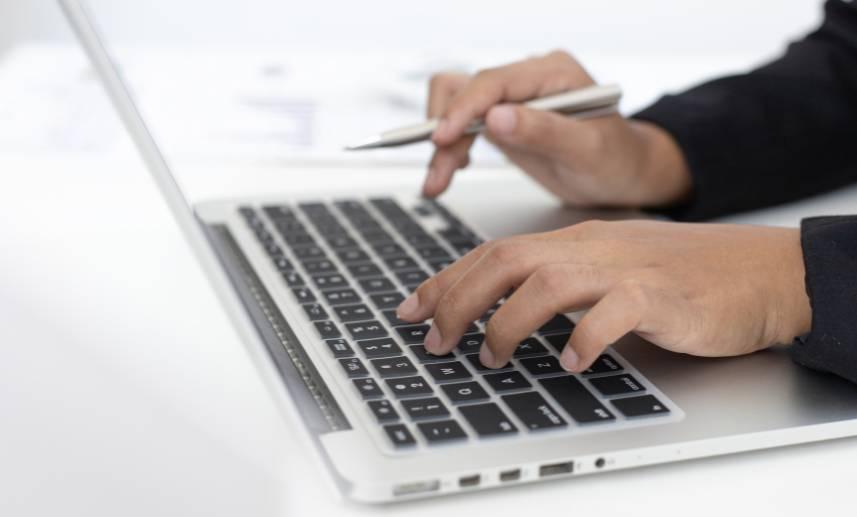 Computadora tipo laptop, sobre su teclado las manos de una persona trabajando.