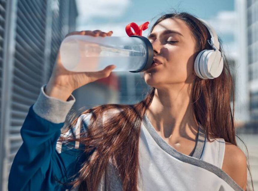 Una mujer aparentemente en actividad física, toma agua.