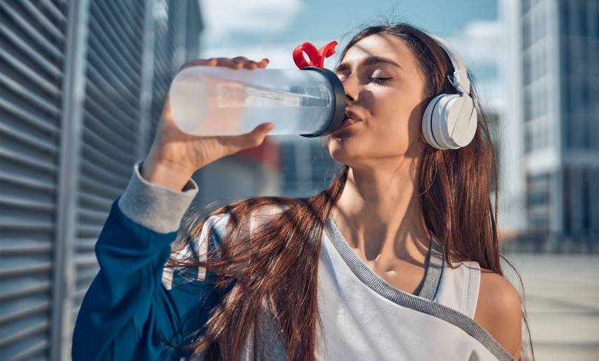 Una mujer aparentemente en actividad física, toma agua.