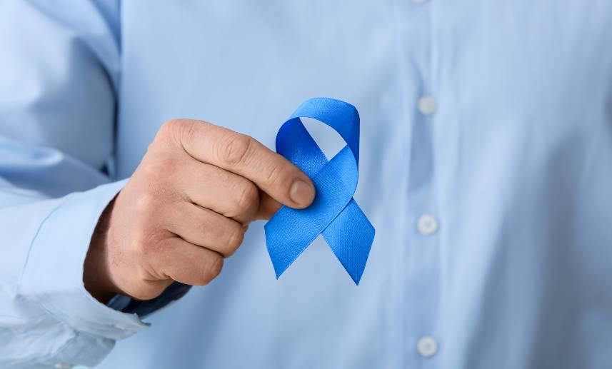 Mano de hombre sostiene un listón azul en señal de apoyo a la lucha contra el cáncer de colón.