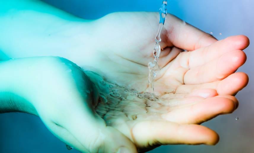 Unas manos reciben agua clara de un chorro, como procedente de una pajilla.