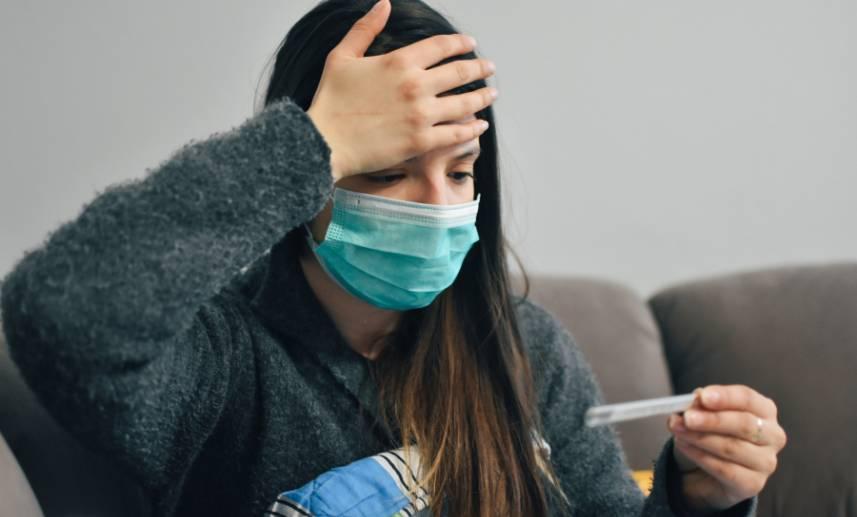 Mujer con cubrebocas se toca la frente viendo una prueba de coronavirus.