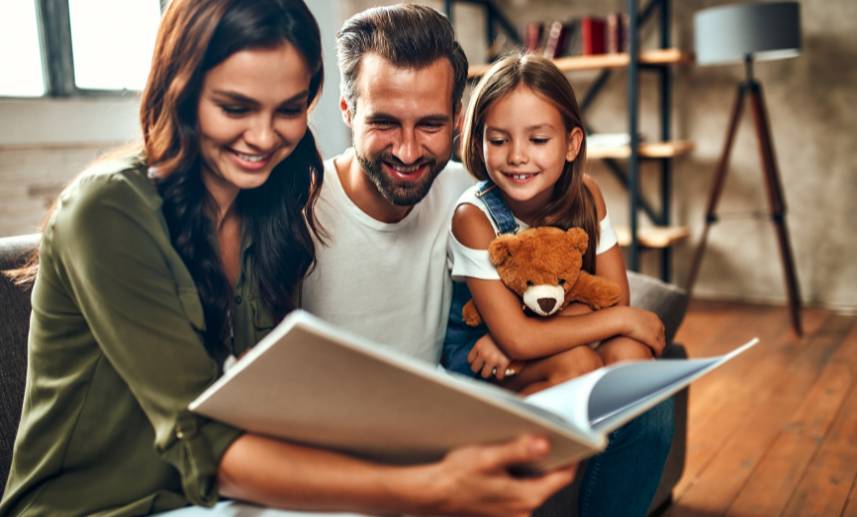 Madre, padre e hija felices leyendo en su sala.