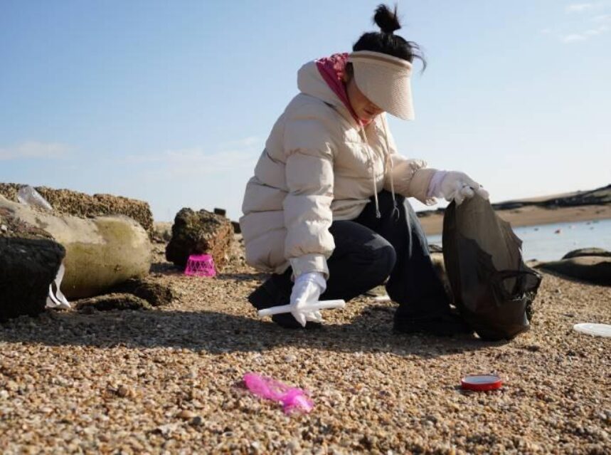 Una mujer recoge basura en una playa.