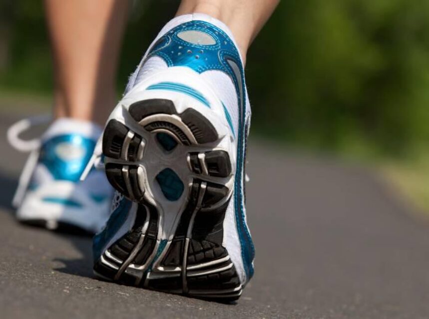 Se ven unos pies con tenis deportivos de correr, caminando en una pista.