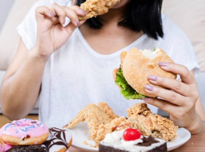 Mujer come comida rápida, con características de ser comida grasosa y alta en calorías.