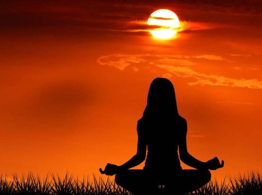 Imagen animada de una mujer de espaldas, haciendo la posición de flor de loto de meditación, mirando al horizonte con una puesta de sol.