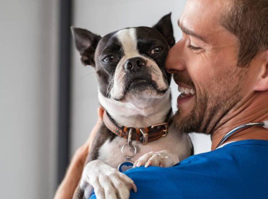 Un hombre con una gran sonrisa en su rostro abraza a un can.