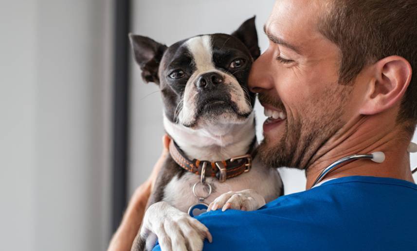 Un hombre con una gran sonrisa en su rostro abraza a un can.