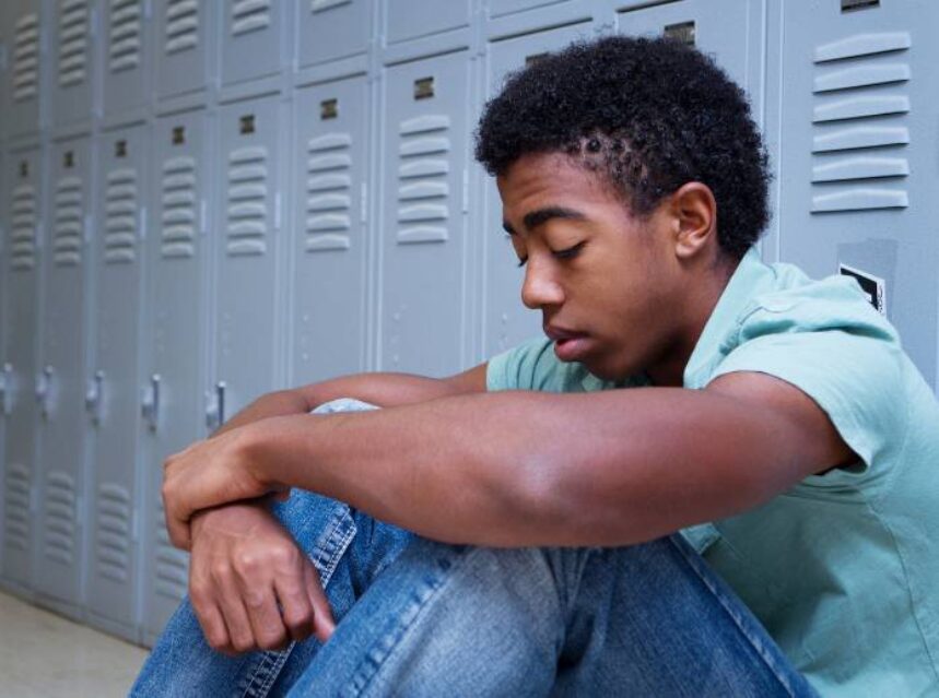 Joven sentado con la mirada hacía el suelo, justo en la zona de lockers de su centro educativo.