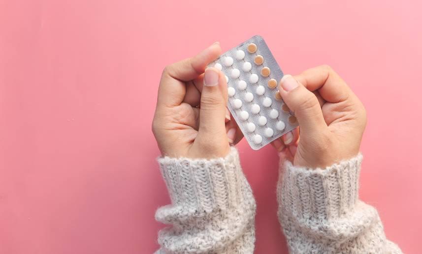 Manos sostienen pastillas anticonceptivas sobre un fondo rosa. ¿Puedo comprar pastillas anticonceptivas sin receta en Estados Unidos? Te contamos lo que debes saber sobre las pastillas anticonceptivas en Estados Unidos.