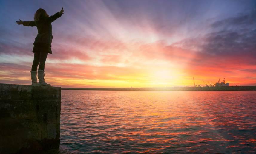 Una mujer abre sus brazos en señal de disfrutar de una puesta de sol. Aprende cómo lidear ocn la depresión.