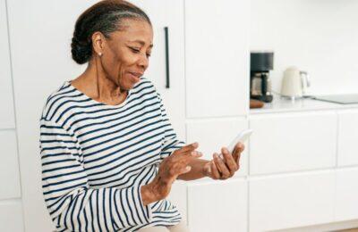 Mujer adulta mayor revisa su dispositivo móvil en la cocina de su casa.