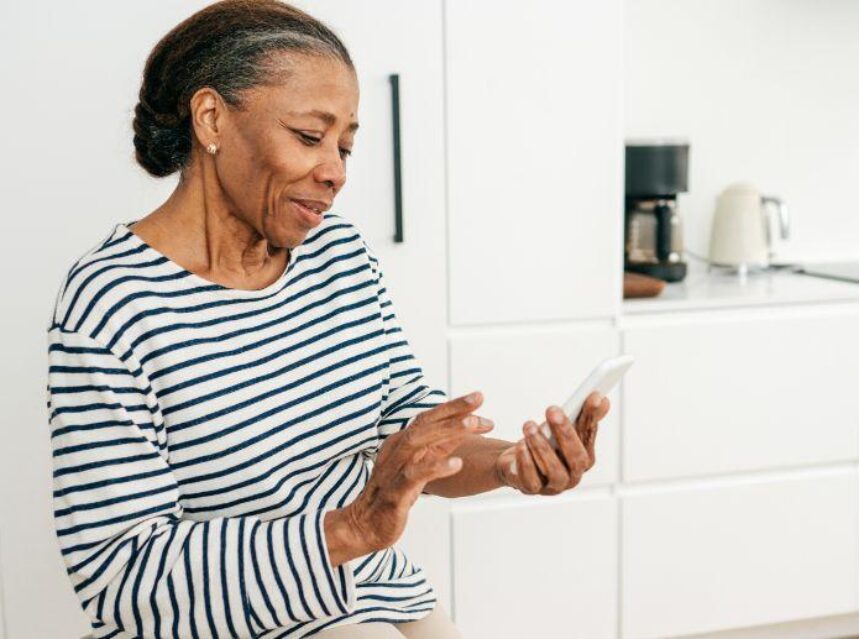 Mujer adulta mayor revisa su dispositivo móvil en la cocina de su casa.