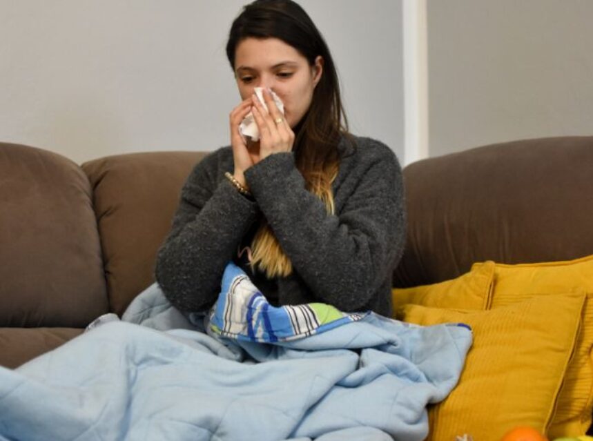 Mujer en sofá visiblemente afectada por un problema respiratorio.