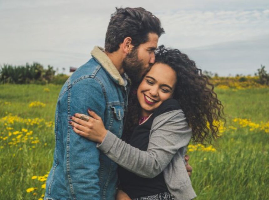 Una pareja se abraza en una pradera, mientras que uno de la un beso en la frente a su pareja.