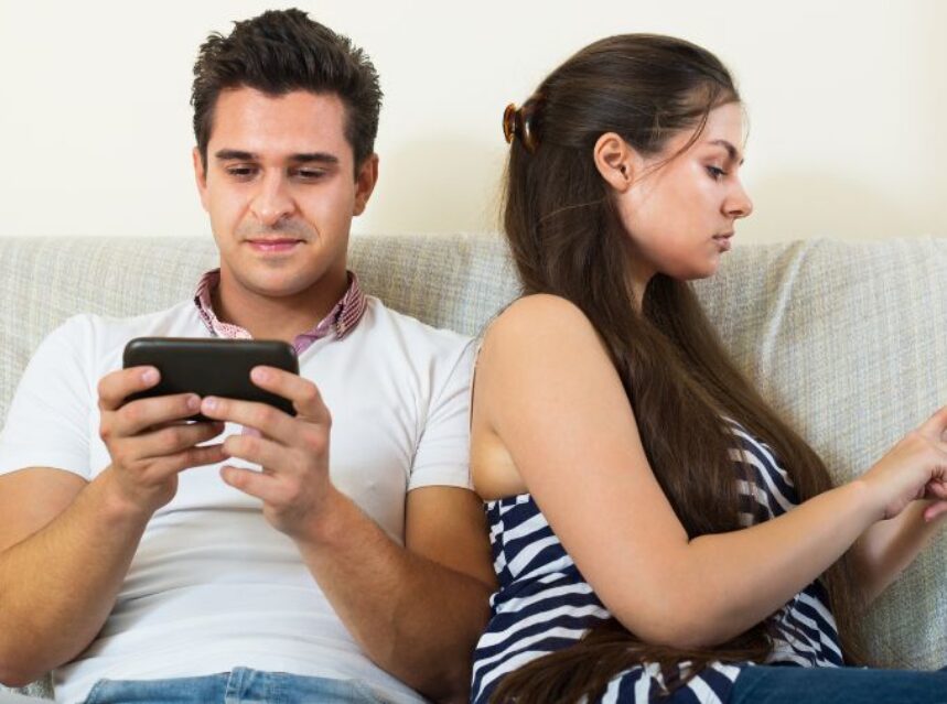 Una pareja en un sofa mira cada uno a su celular.