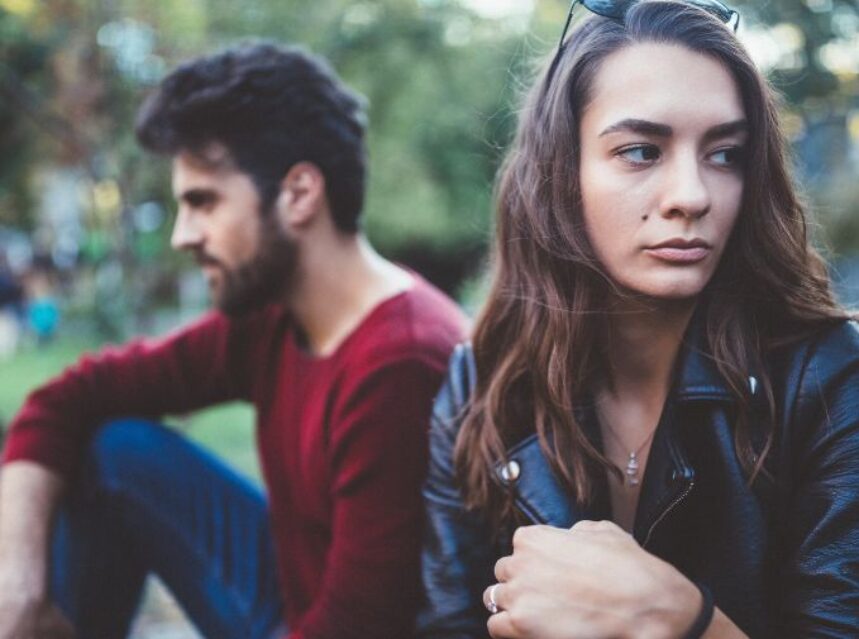 Un joven hombre y una joven mujer se dan la espalda, sentados en un parque.