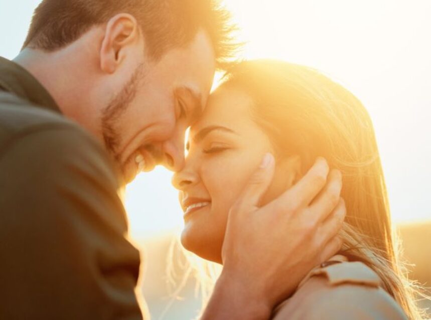 Pareja une sus rostros sonrientes con un sol resplandeciente de fondo.