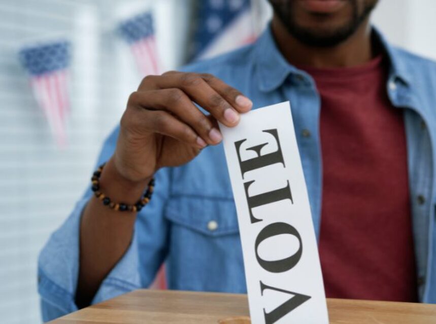 Un joven hombre deposita un documento que dice "Vote" en una urna.