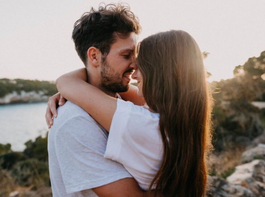 Una pareja se abraza amorosamente con un paisaje de naturaleza detrás.