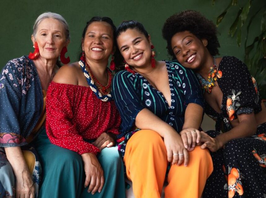 Cuatro mujeres empoderadas sonrién mientras comparten el asiento en un sofá.