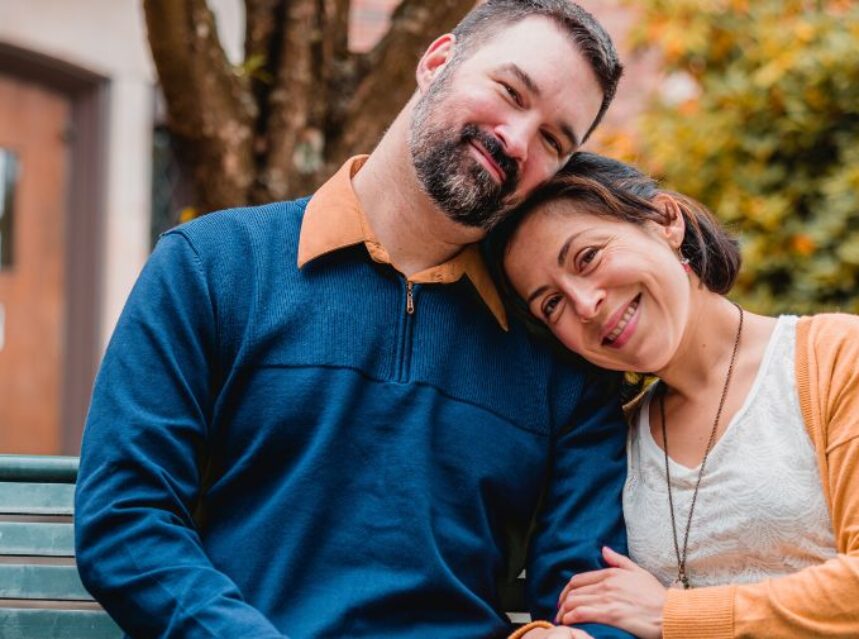 Pareja en una banca de un parque sonrientes y acurrucados.