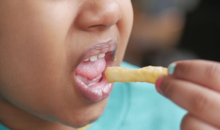 Rostro parcial de una niña mientras lleva una papa frita a su boca.