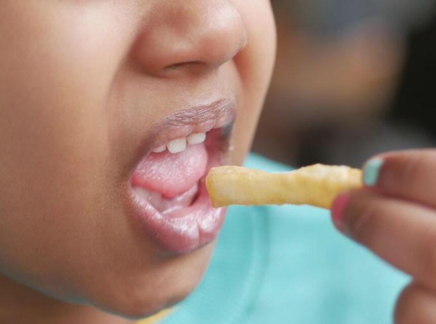 Rostro parcial de una niña mientras lleva una papa frita a su boca.