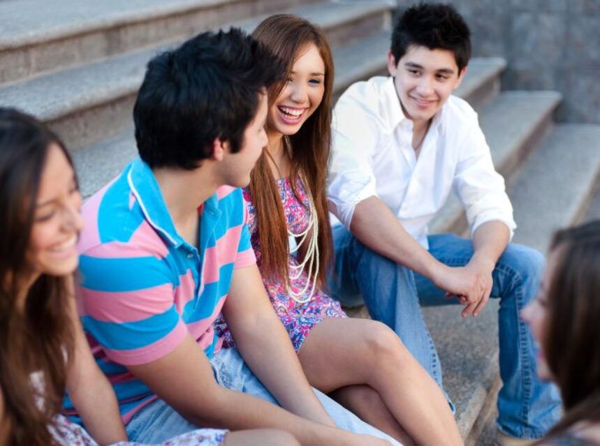 Jóvenes sonrientes sentados en una escalera, mientras conversan.