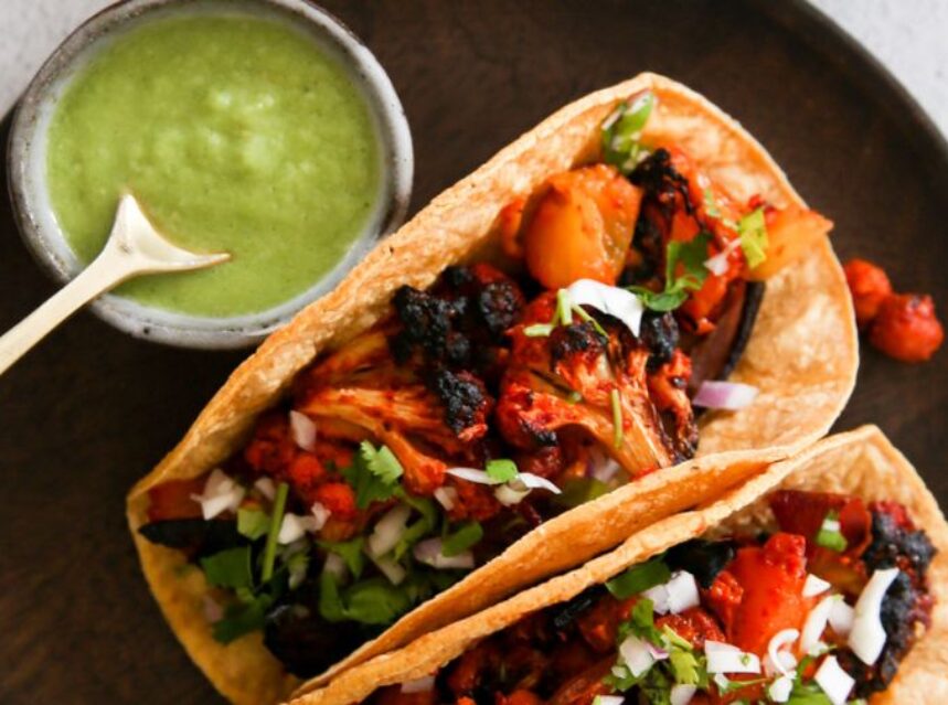 Dos tacos de coliflor al pastor con una salsa verde a un lado.