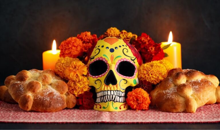 Altar de muertos, dos veladoras, flores, dos panes de muertos y una calavera al centro.